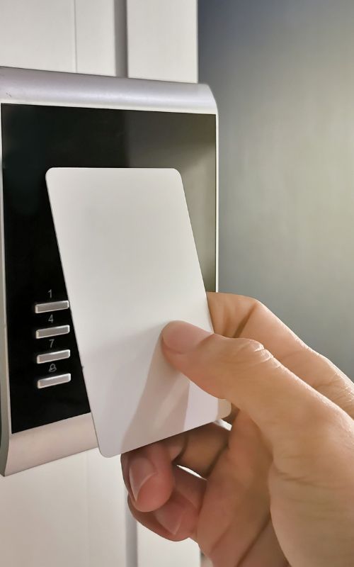 Hand inserting a white card into a black wall-mounted access card reader with silver trim