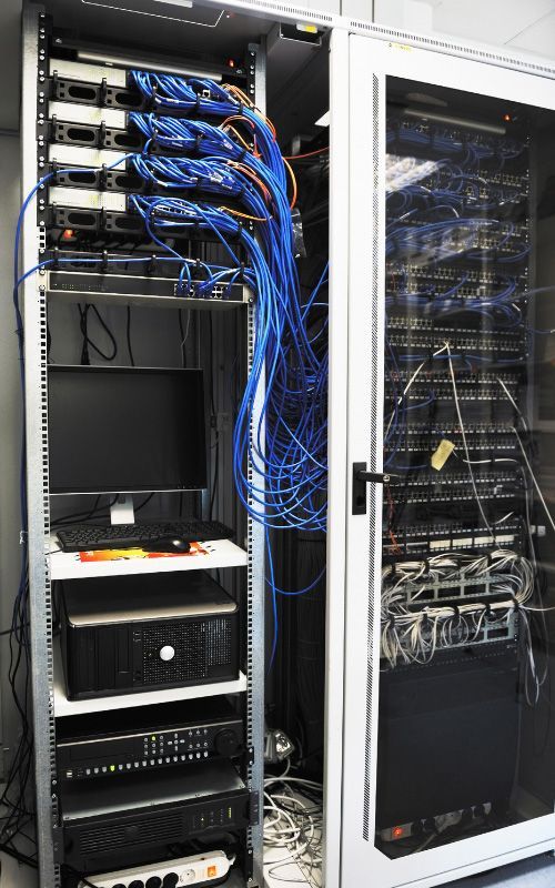 Open server rack with blue network cables beside a closed glass data cabinet