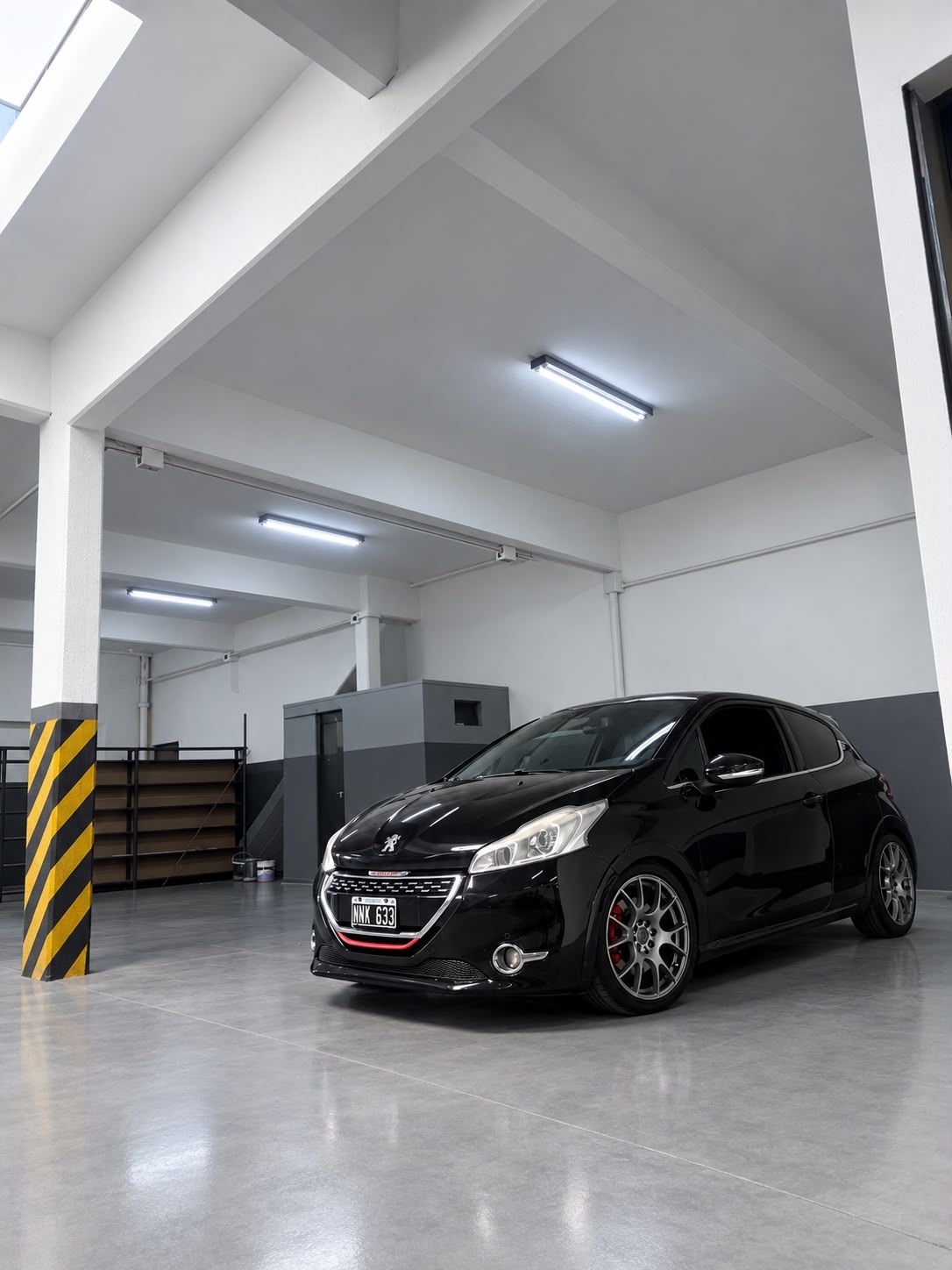 Hatchback negro estacionado en un garaje interior luminoso, con paredes blancas y una columna con franjas amarillas y negras