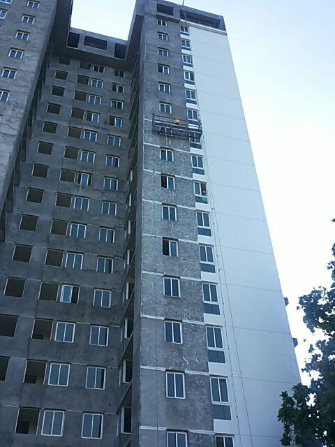A high-rise building under construction, showing a contrast between the unfinished gray facade and a painted white section.