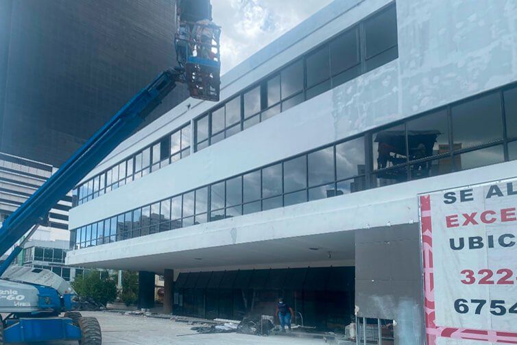 A blue construction lift parked in front of a white multi-story office building undergoing exterior renovations.