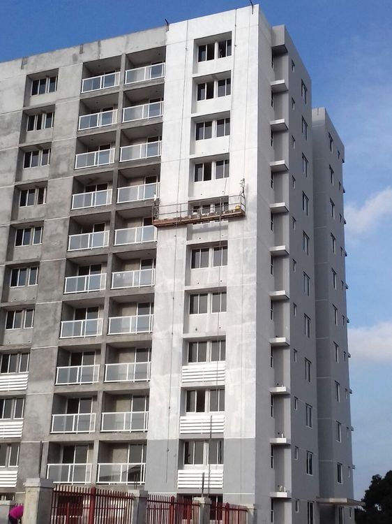 A high-rise apartment building under construction, featuring white painted sections and workers on a suspended scaffold.