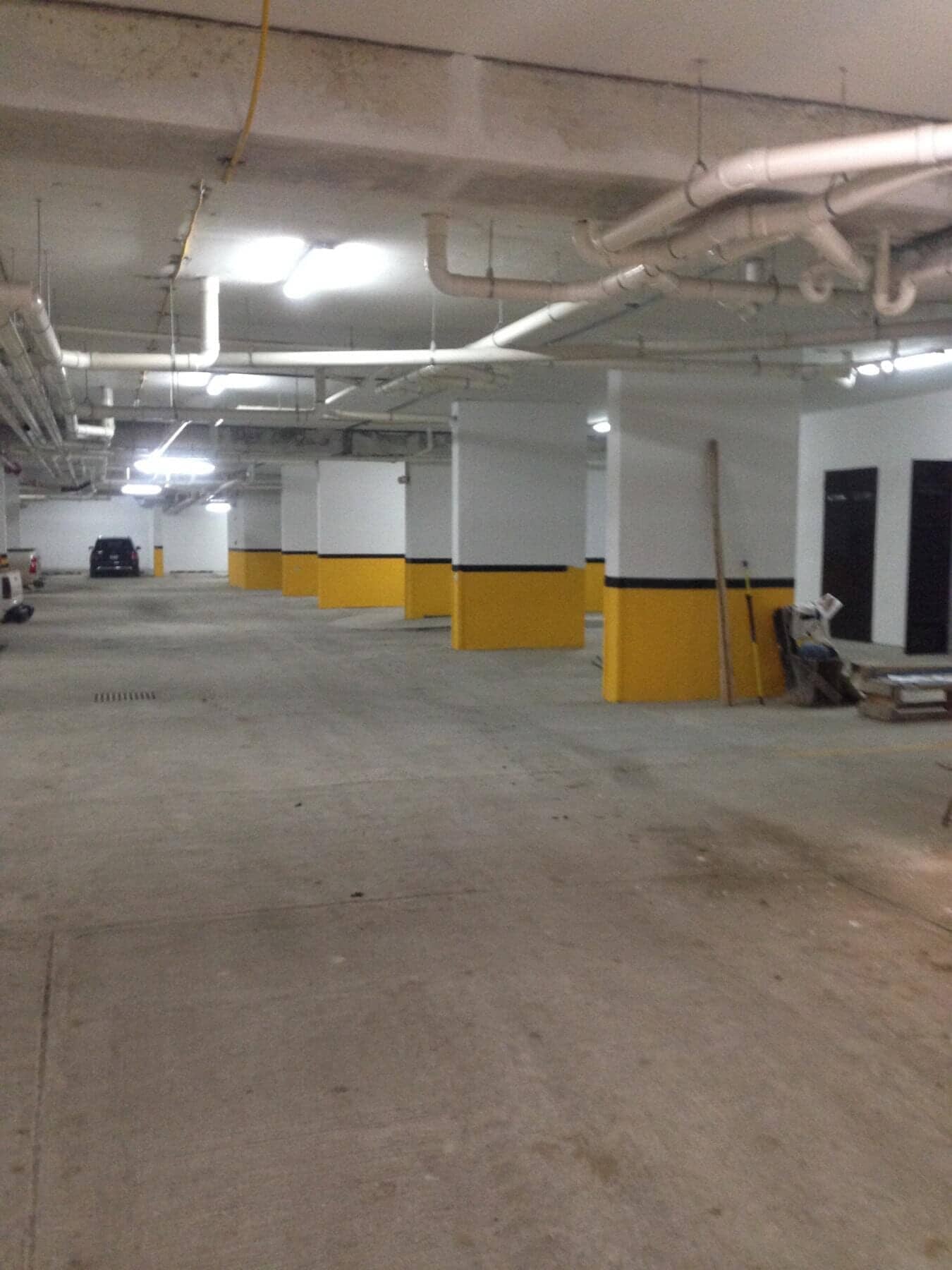An empty parking garage with white and yellow pillars and exposed pipes along the ceiling.
