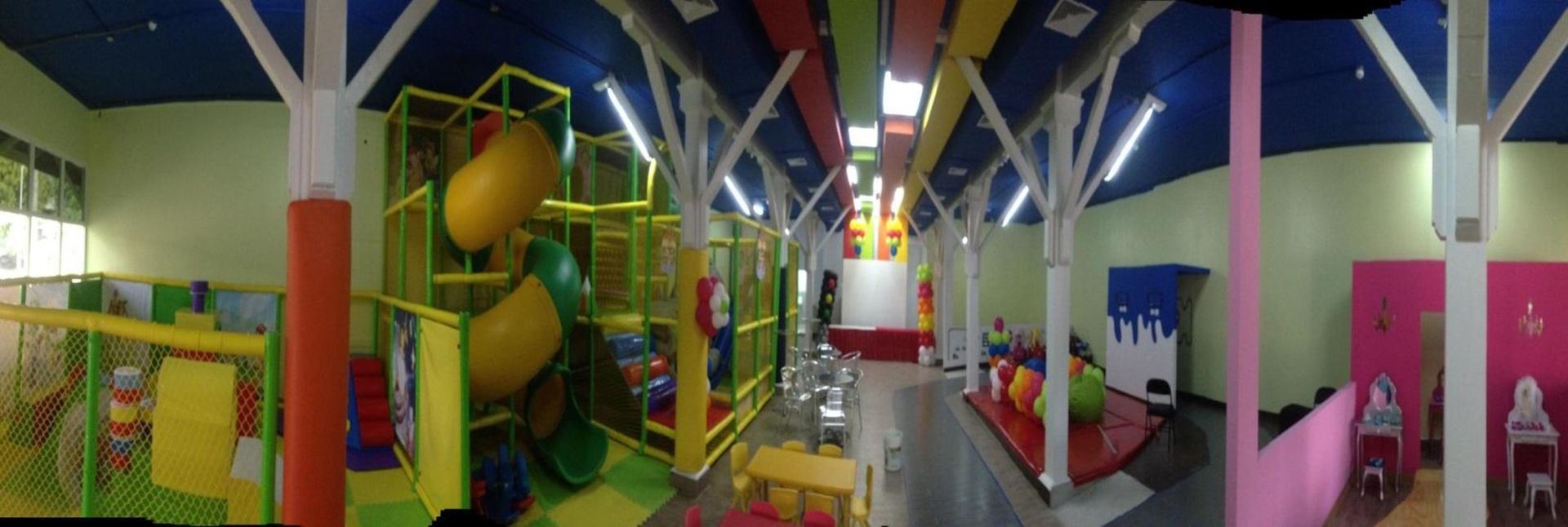 A panoramic view of an indoor children's playground featuring a multi-level climbing structure, slides, and seating area.
