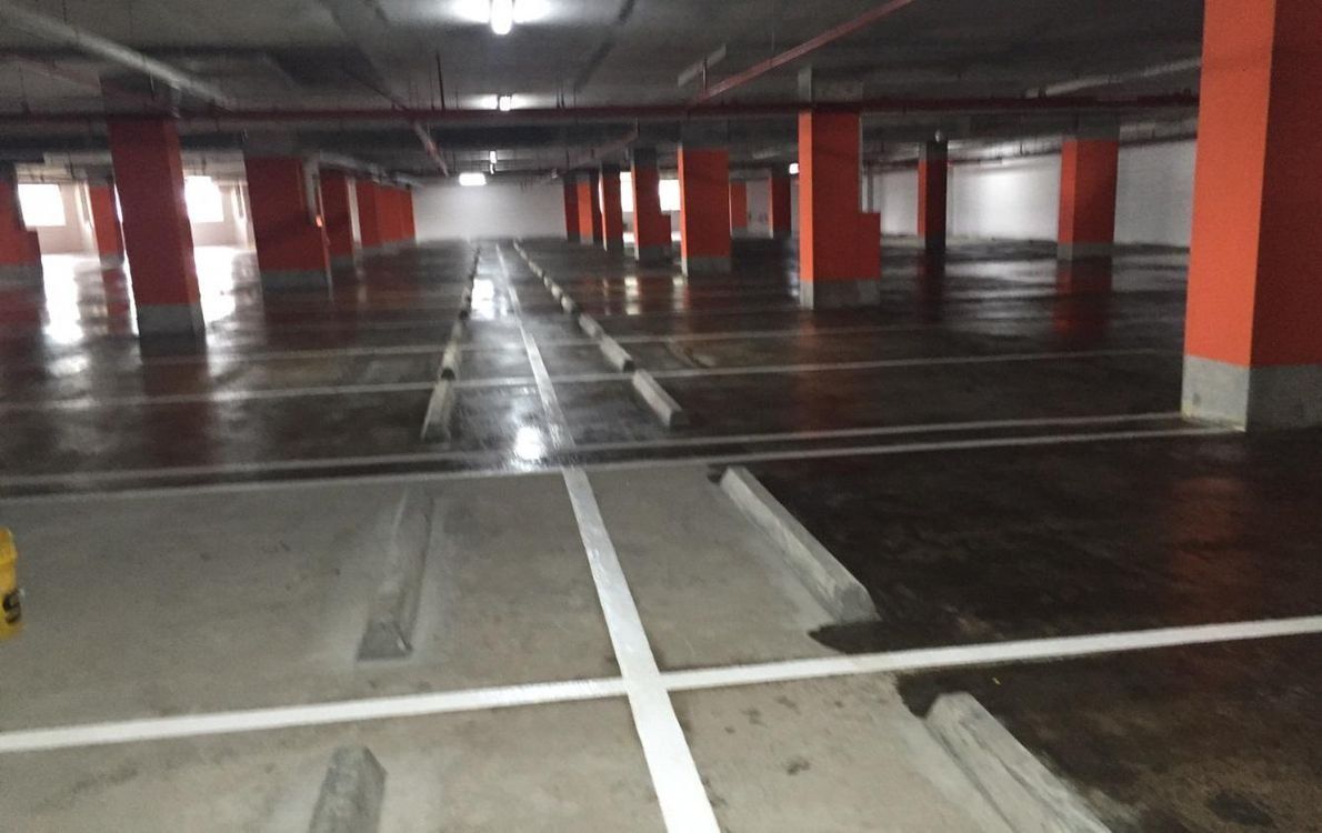 An empty underground parking garage with orange pillars, concrete floors, and white painted parking space markings.