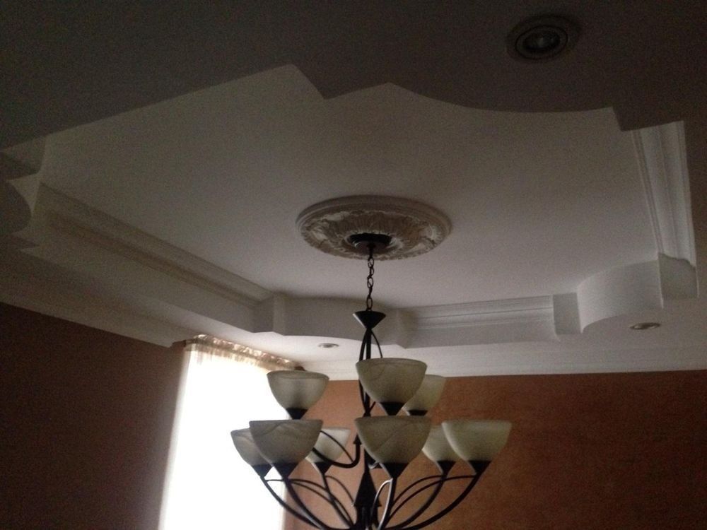 A modern chandelier hangs below a decorative, recessed tray ceiling with ornate molding and a ceiling medallion.