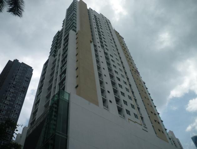 A tall, modern residential skyscraper with white and tan panels under a cloudy sky, next to a darker building.