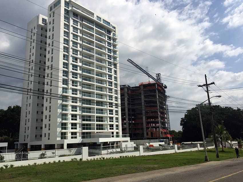 A tall, white apartment building stands next to a skeletal, under-construction high-rise under a cloudy sky.
