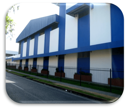 A building with a blue and white striped exterior, bordered by a black metal fence and a roadside sidewalk.