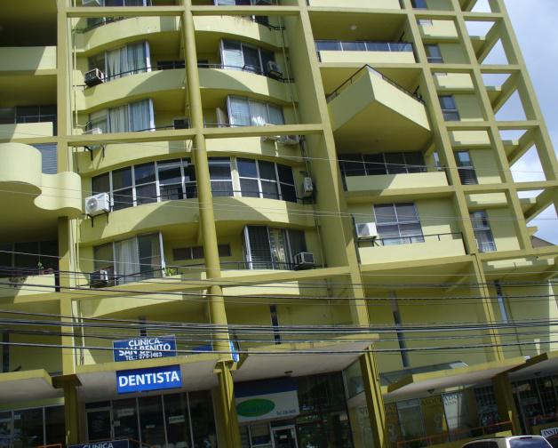 A multistory, light-green apartment building with external balconies and a ground-floor dentist's office with a sign.