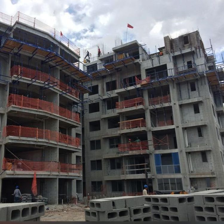Multi-story concrete apartment buildings under construction with orange safety netting and workers on site.