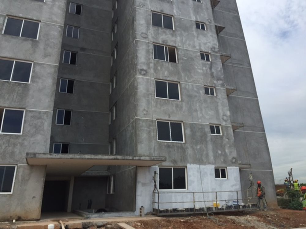 A modern gray multi-story apartment building under construction, with a worker on a lift platform near the ground floor.