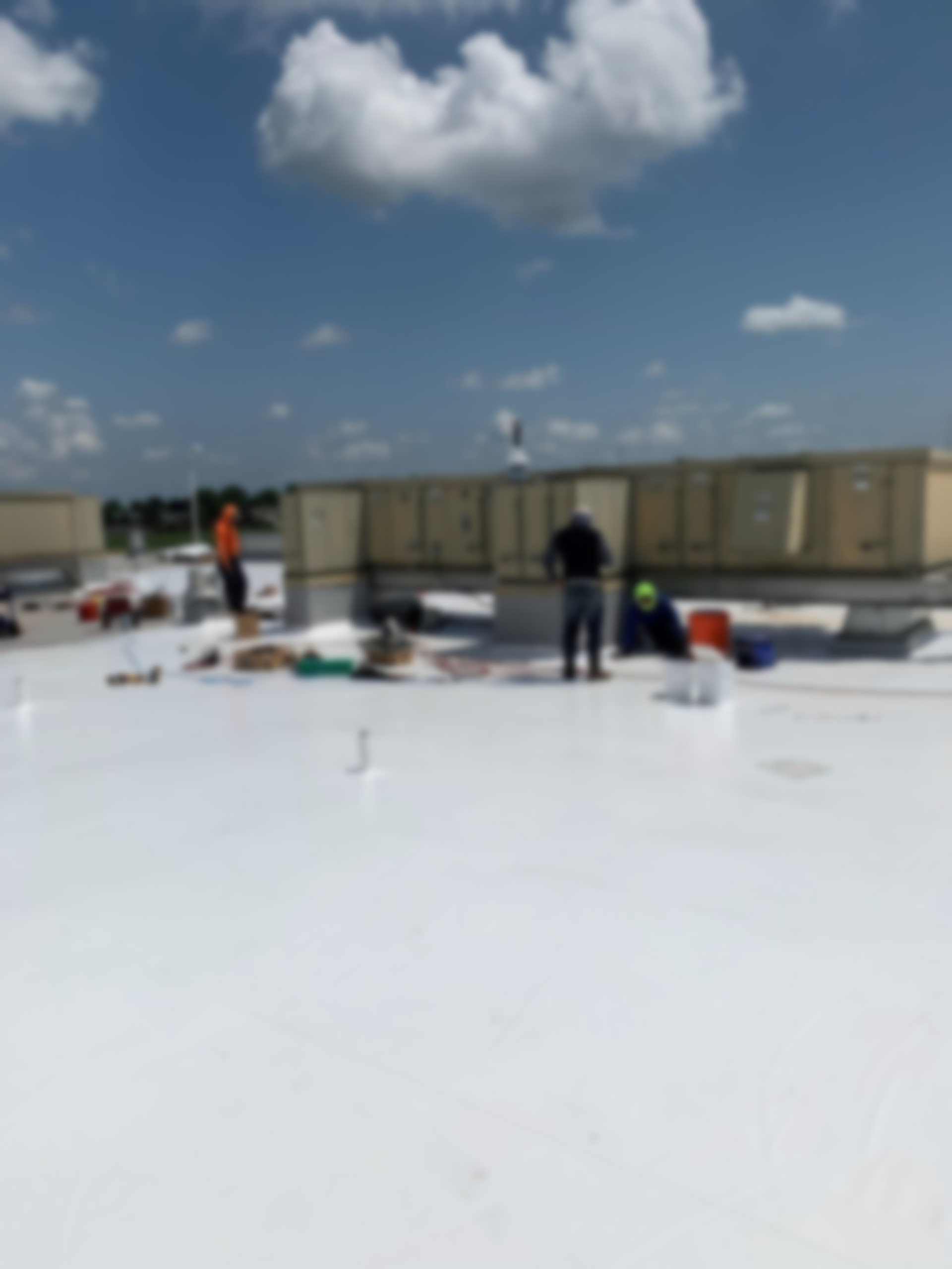 Aerial view of construction workers installing a black membrane roof on a multi-story concrete apartment building.