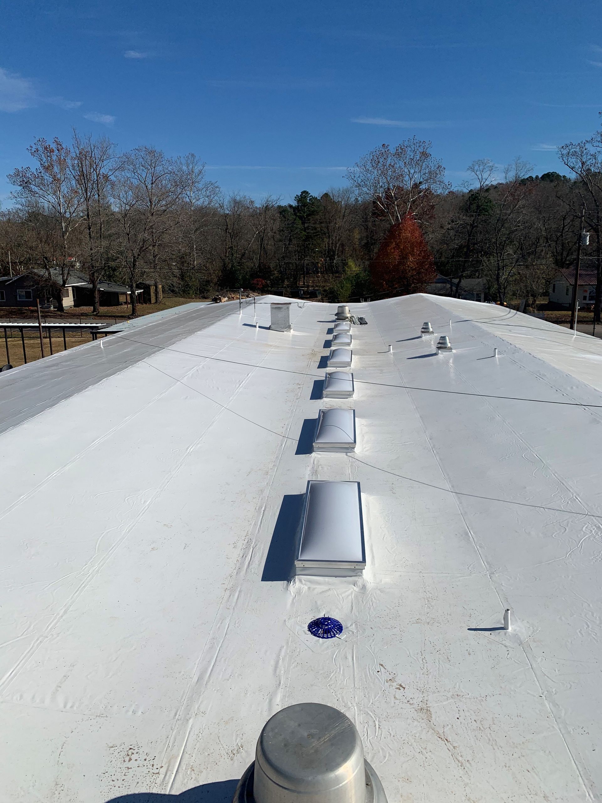 White rooftop with rows of skylights under a clear blue sky