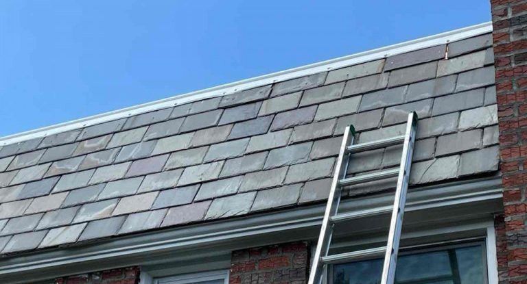 a ladder is sitting on the new slate roof of a house .