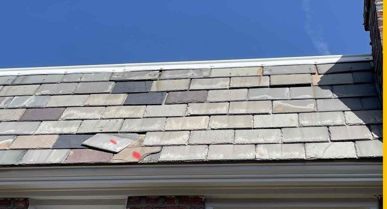 a close up of a damaged slate roof with a blue sky in the background