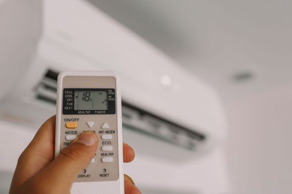 Hand holding a remote pointed at a wall-mounted air conditioner in a room