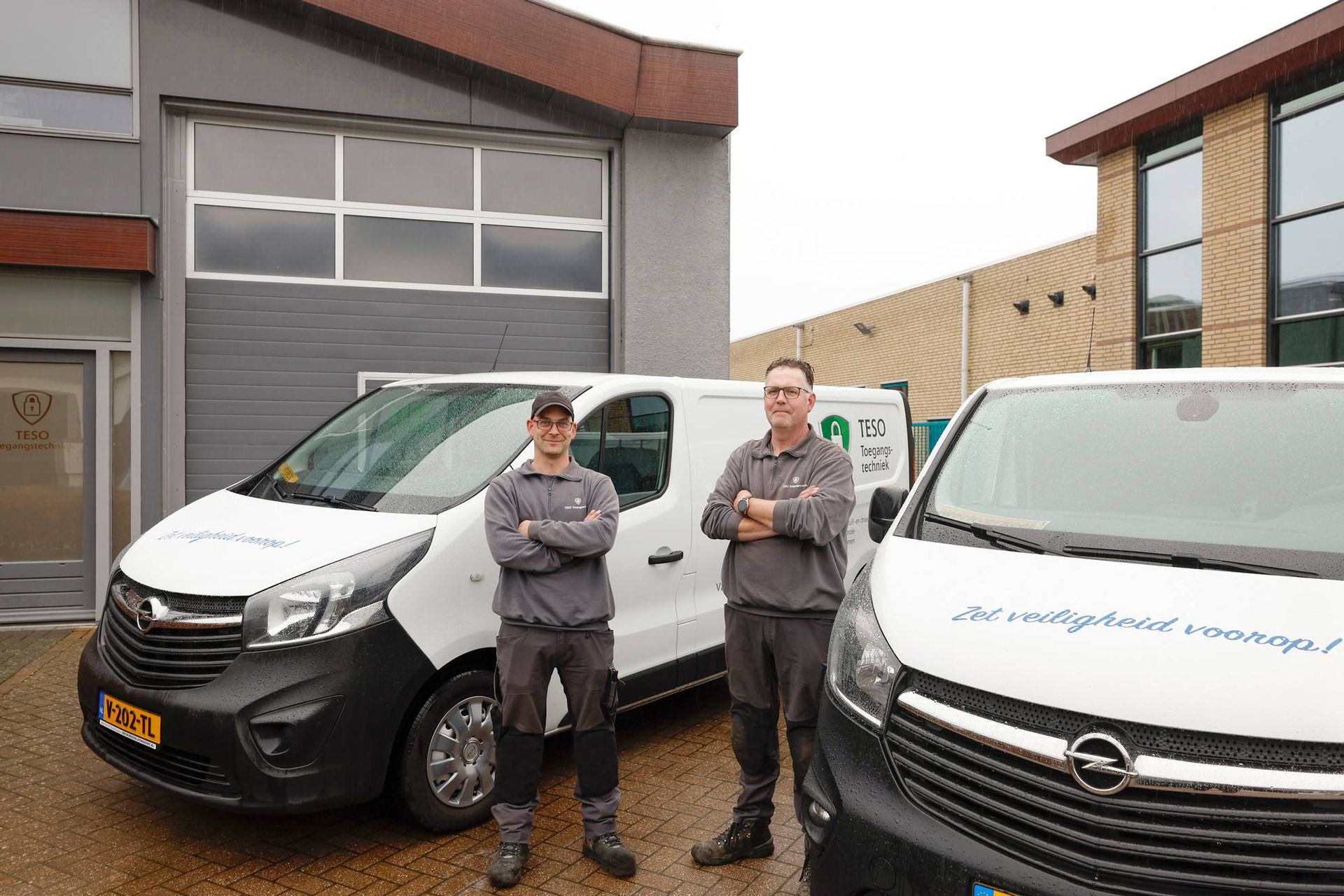 Twee mannen staan naast twee busjes voor een gebouw.
