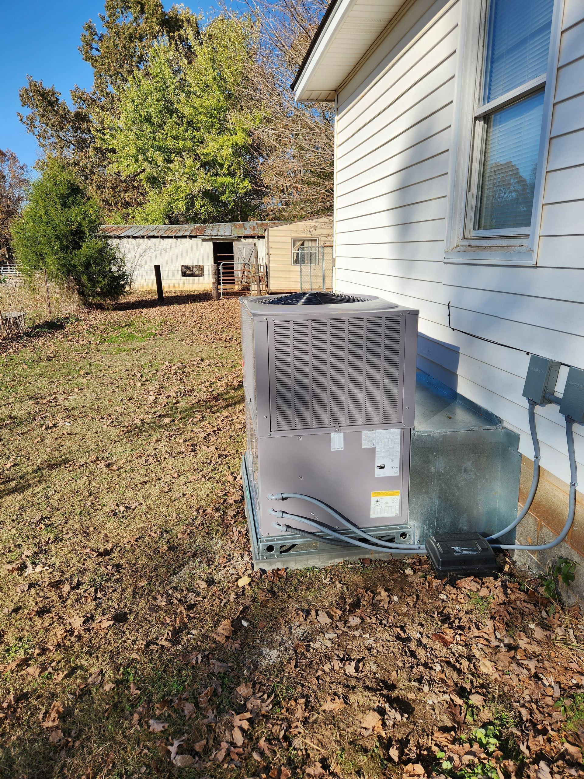Outdoor HVAC unit beside a white house with autumn leaves and trees in the yard