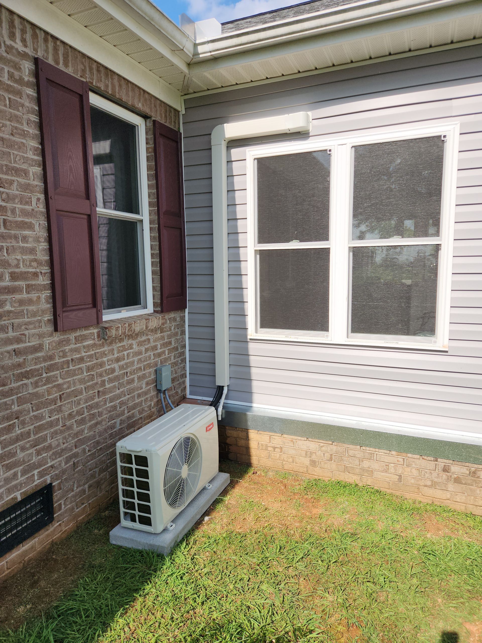 Side of a house with brick and white siding, a window, and a small air conditioner unit by the wall.