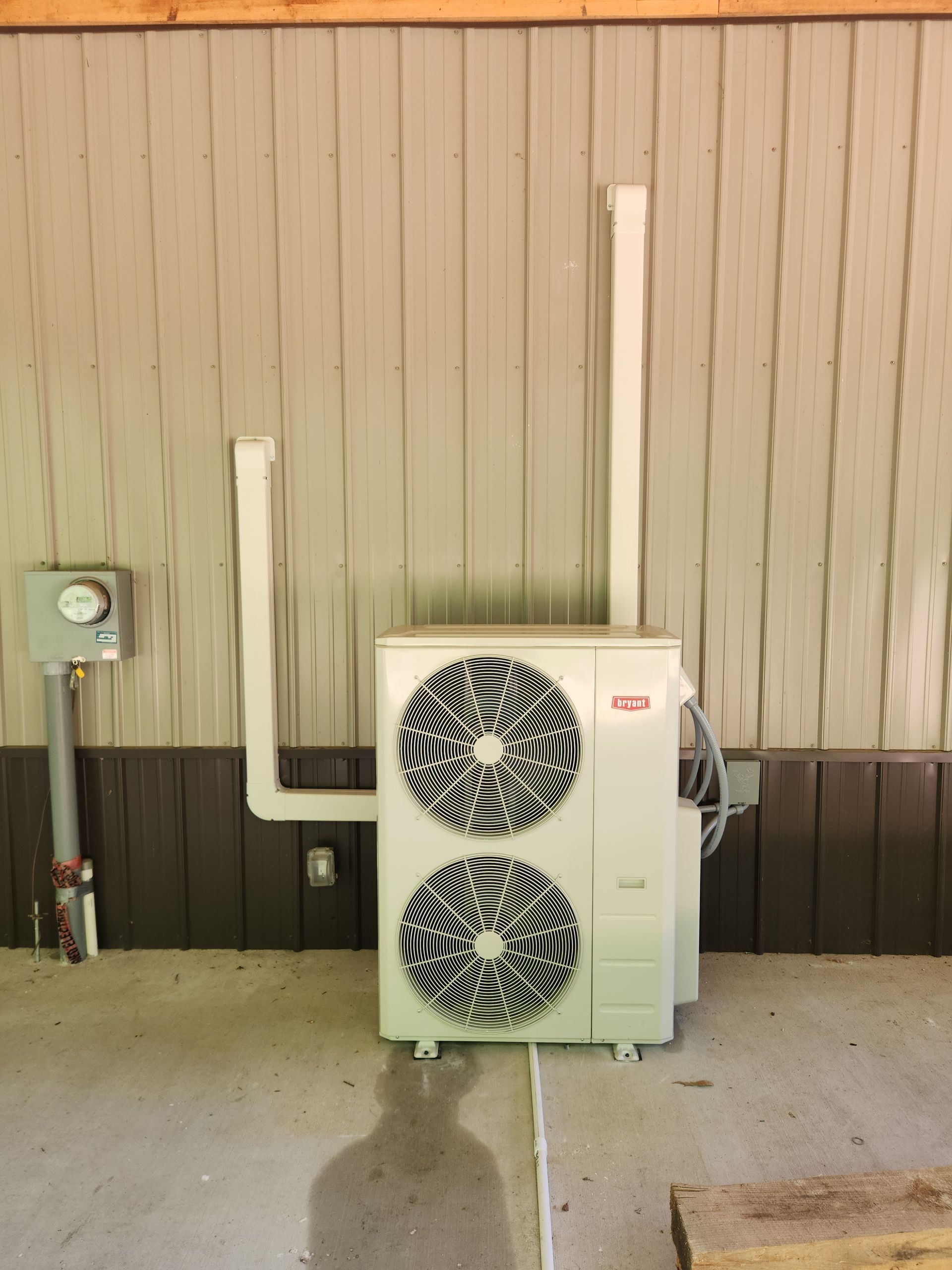 Outdoor wall-mounted HVAC unit with two fan grilles beside a beige building wall and utility boxes