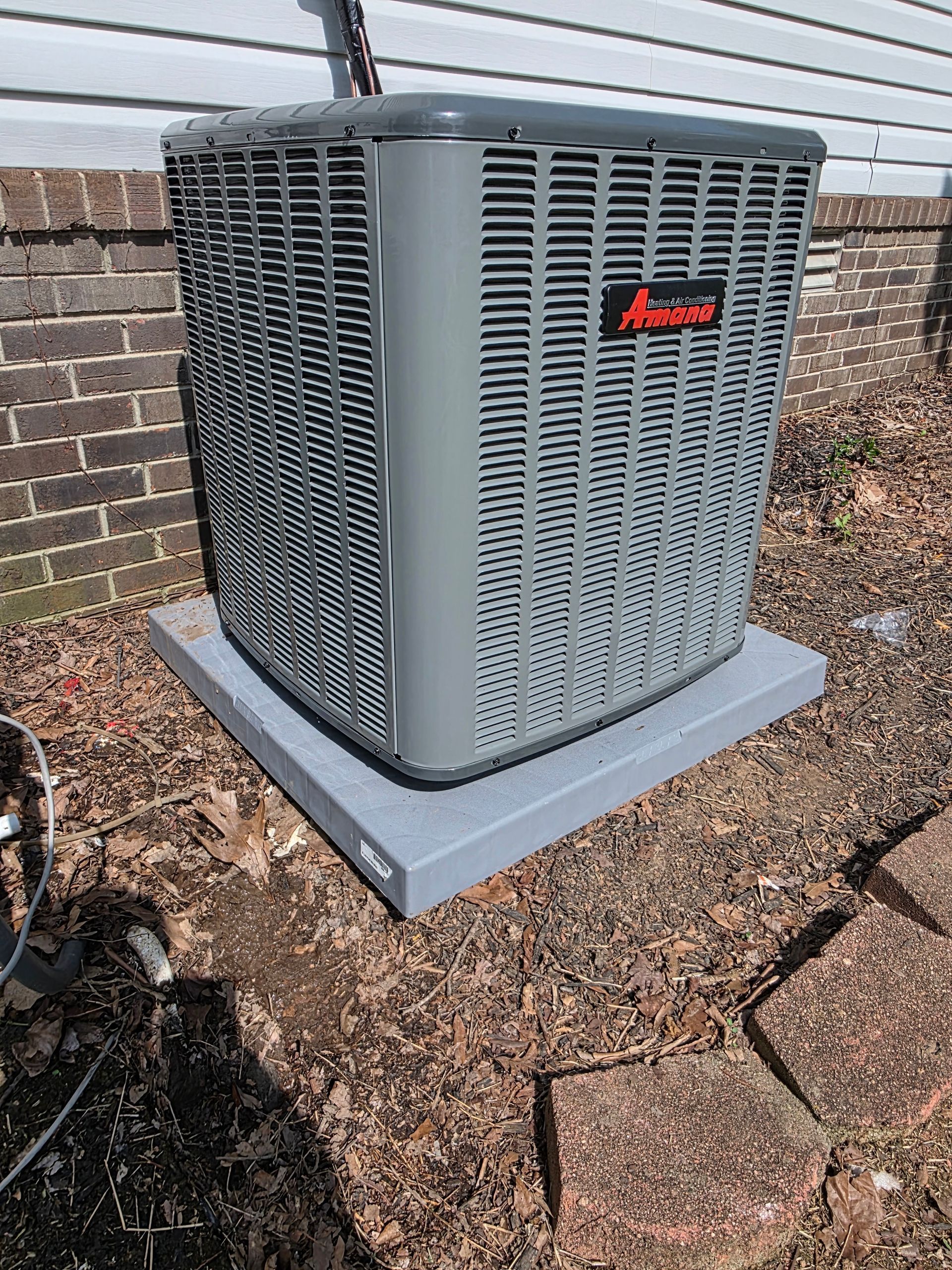 Outdoor air conditioning unit on a concrete pad beside a brick wall.