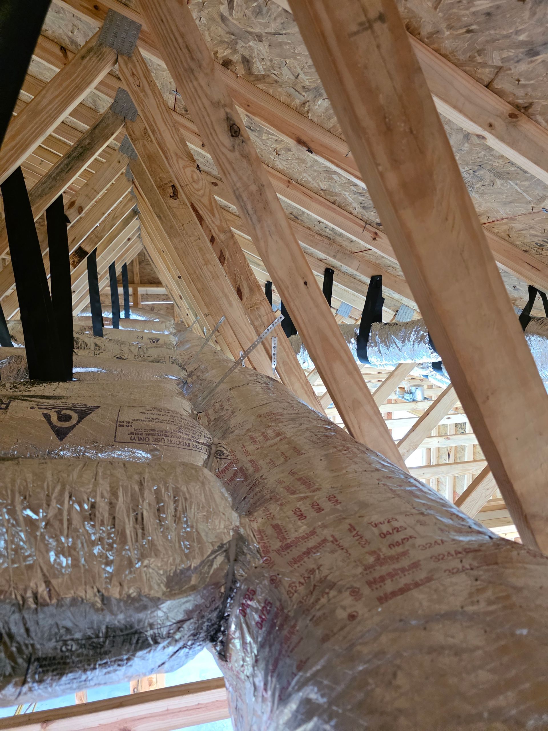 Metal HVAC ductwork installed in a wooden attic ceiling with exposed beams and skylight light
