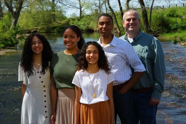 Five people smiling and standing together beside a river on a sunny day