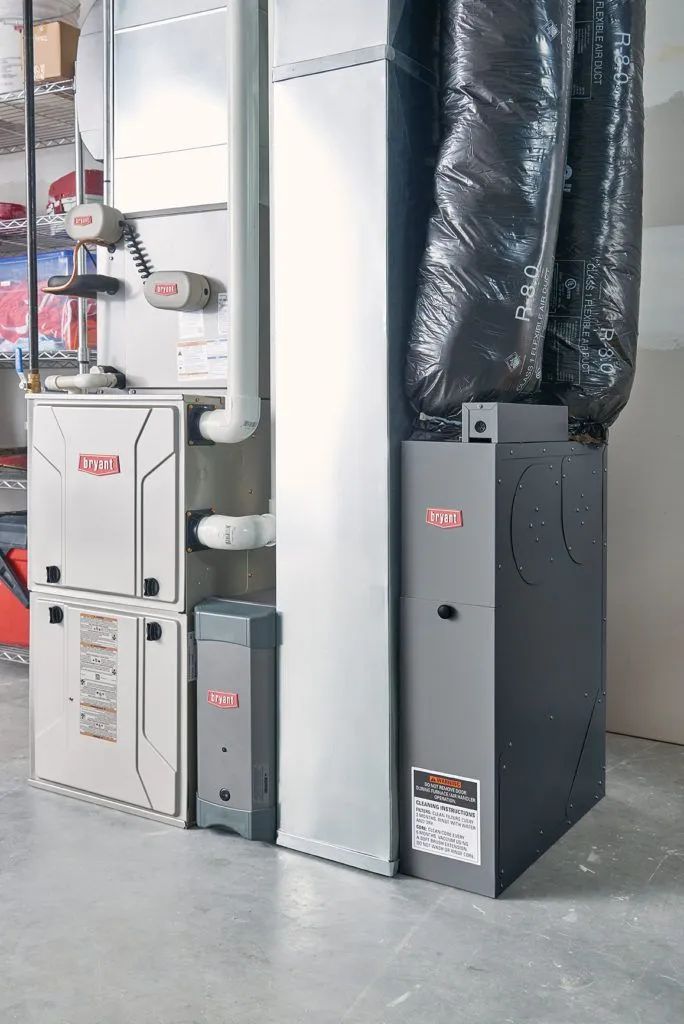 HVAC furnace units and ductwork in a utility room with exposed pipes and concrete floor
