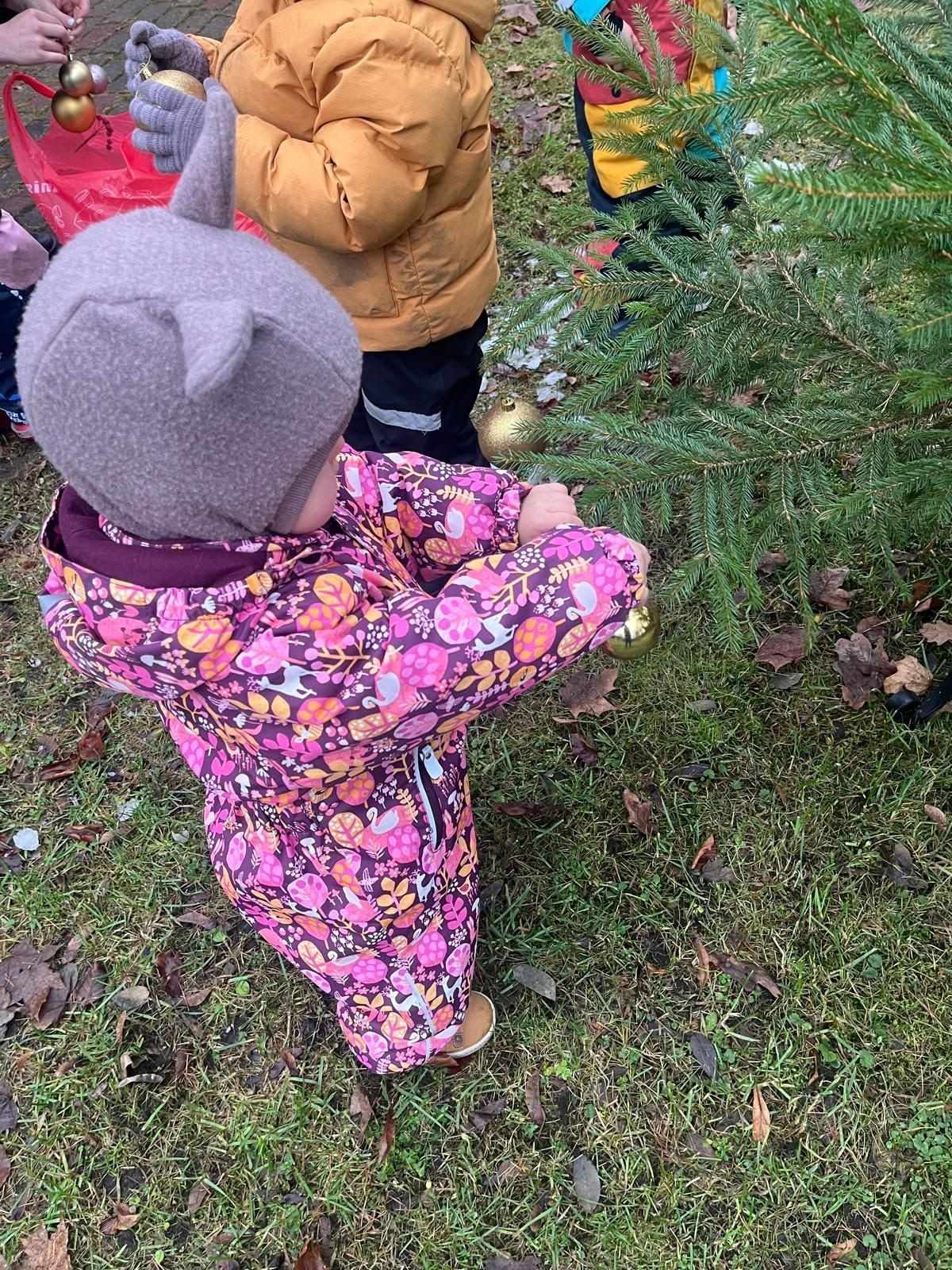 Divi bērni krāsainos ziemas mēteļos pēta izrotātu āra mūžzaļo koku