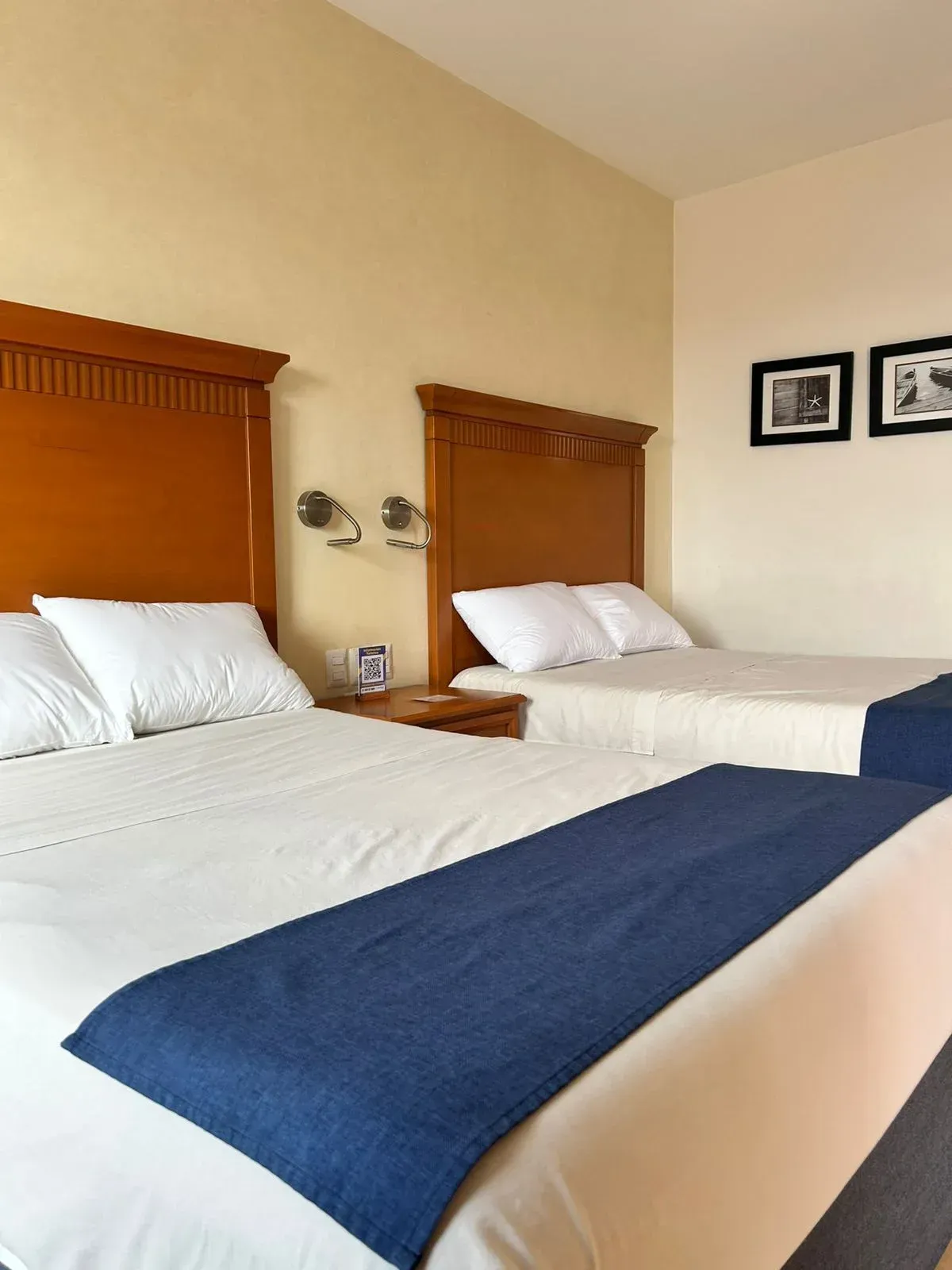 Dos camas de hotel con sábanas blancas, caminos de mesa azules y cabeceros de madera.