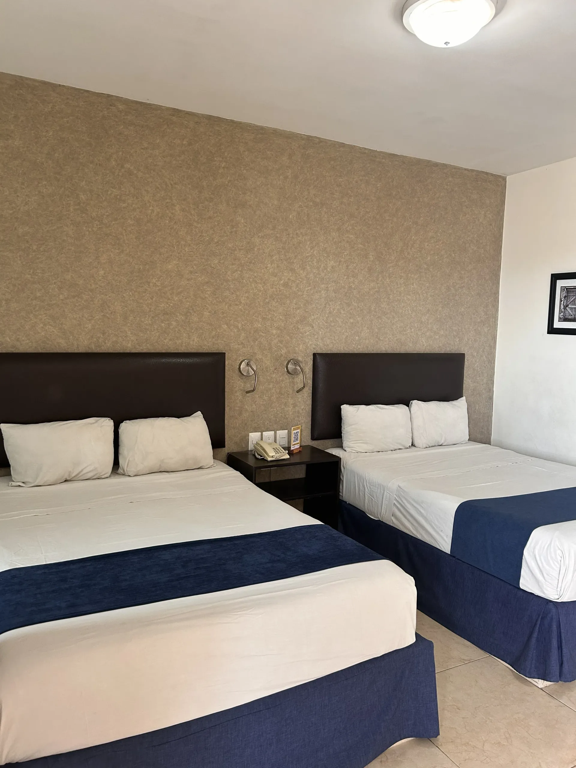 Una habitación de hotel con dos camas tamaño queen, cabeceros oscuros, sábanas blancas con caminos de mesa azul marino.