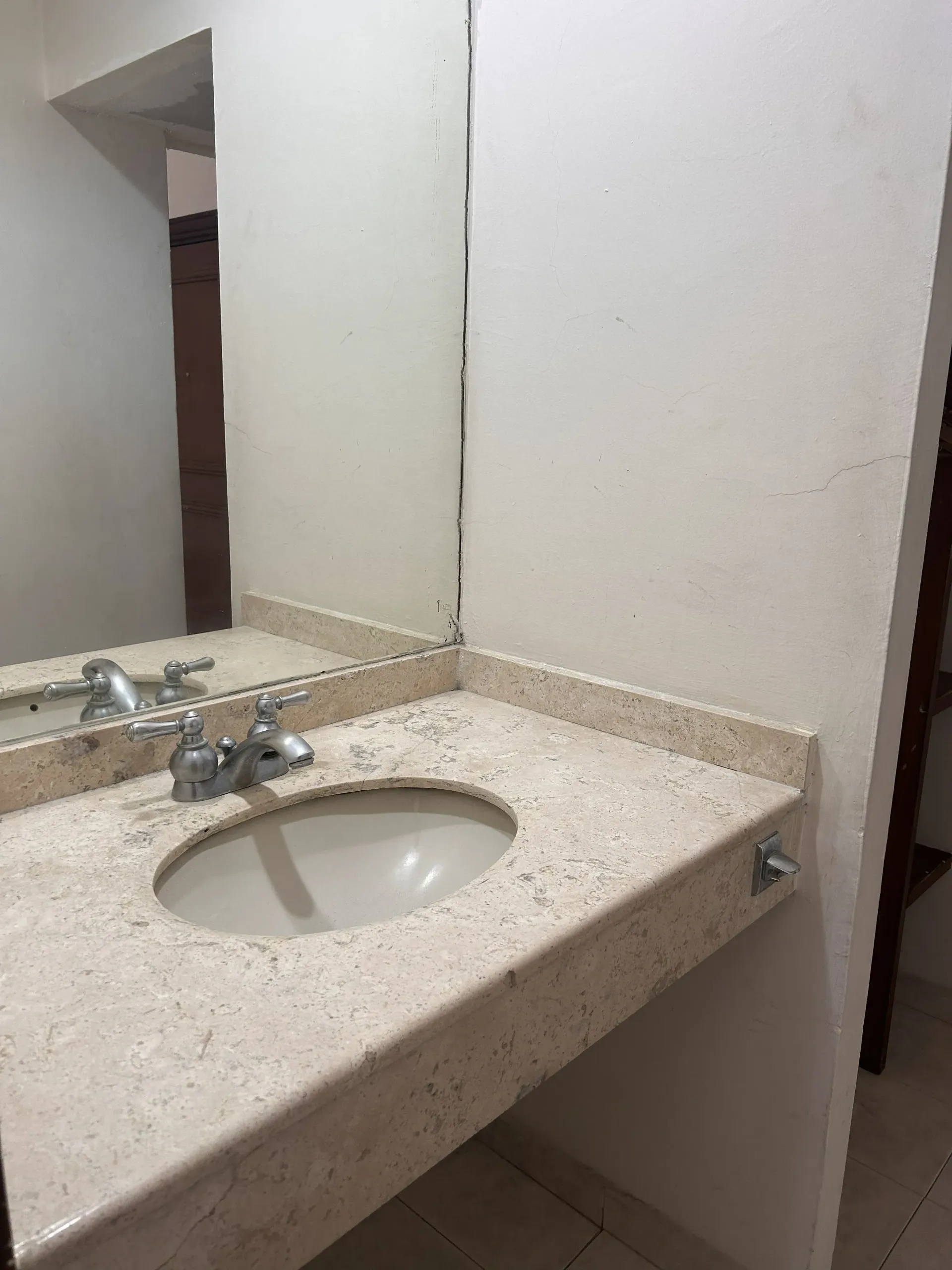 Un mueble de baño con encimera de piedra beige moteada, lavabo ovalado empotrado, grifo cromado y un espejo grande.