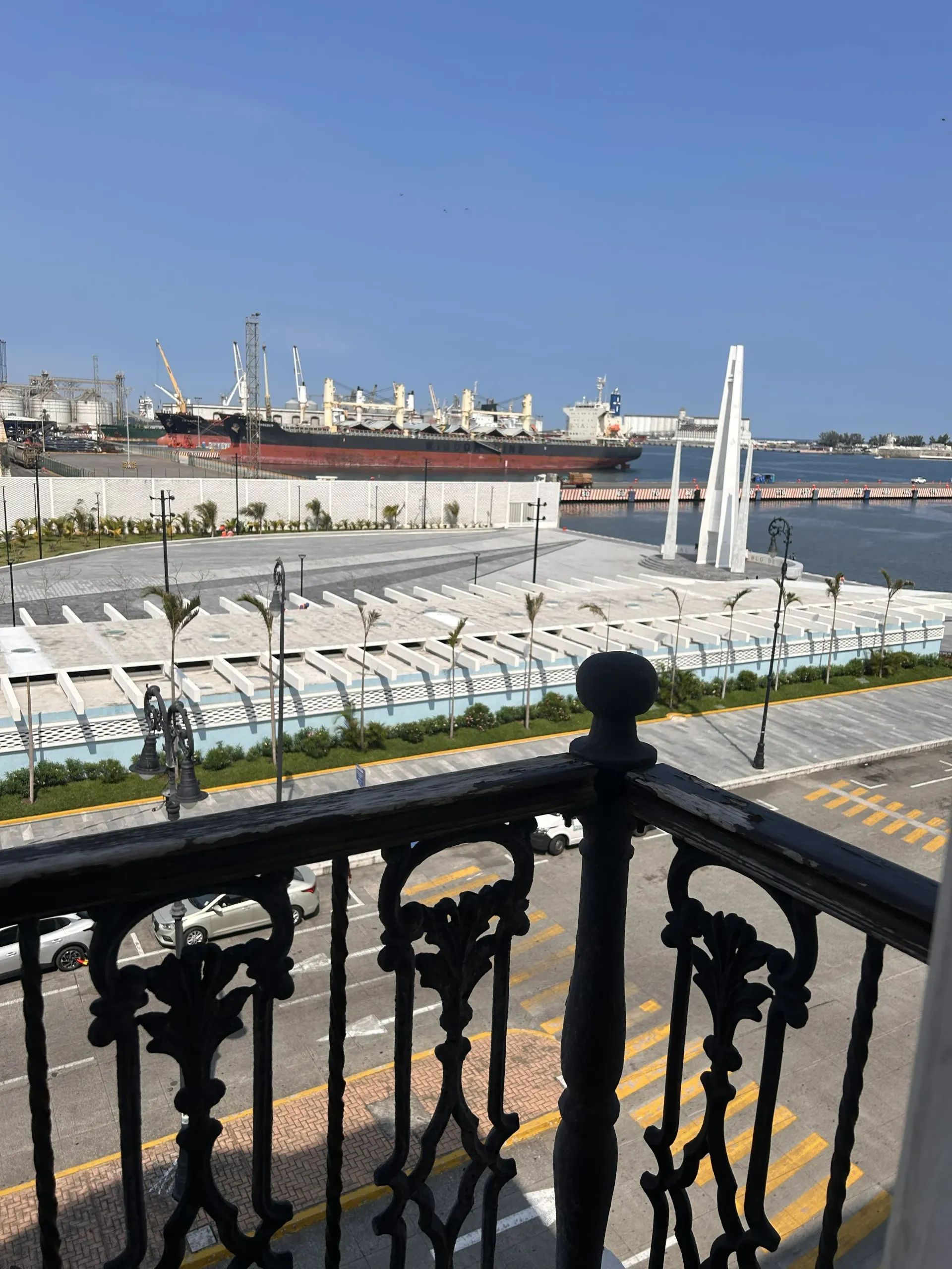 Vista desde un balcón que da a una plaza pavimentada con una alta escultura blanca.