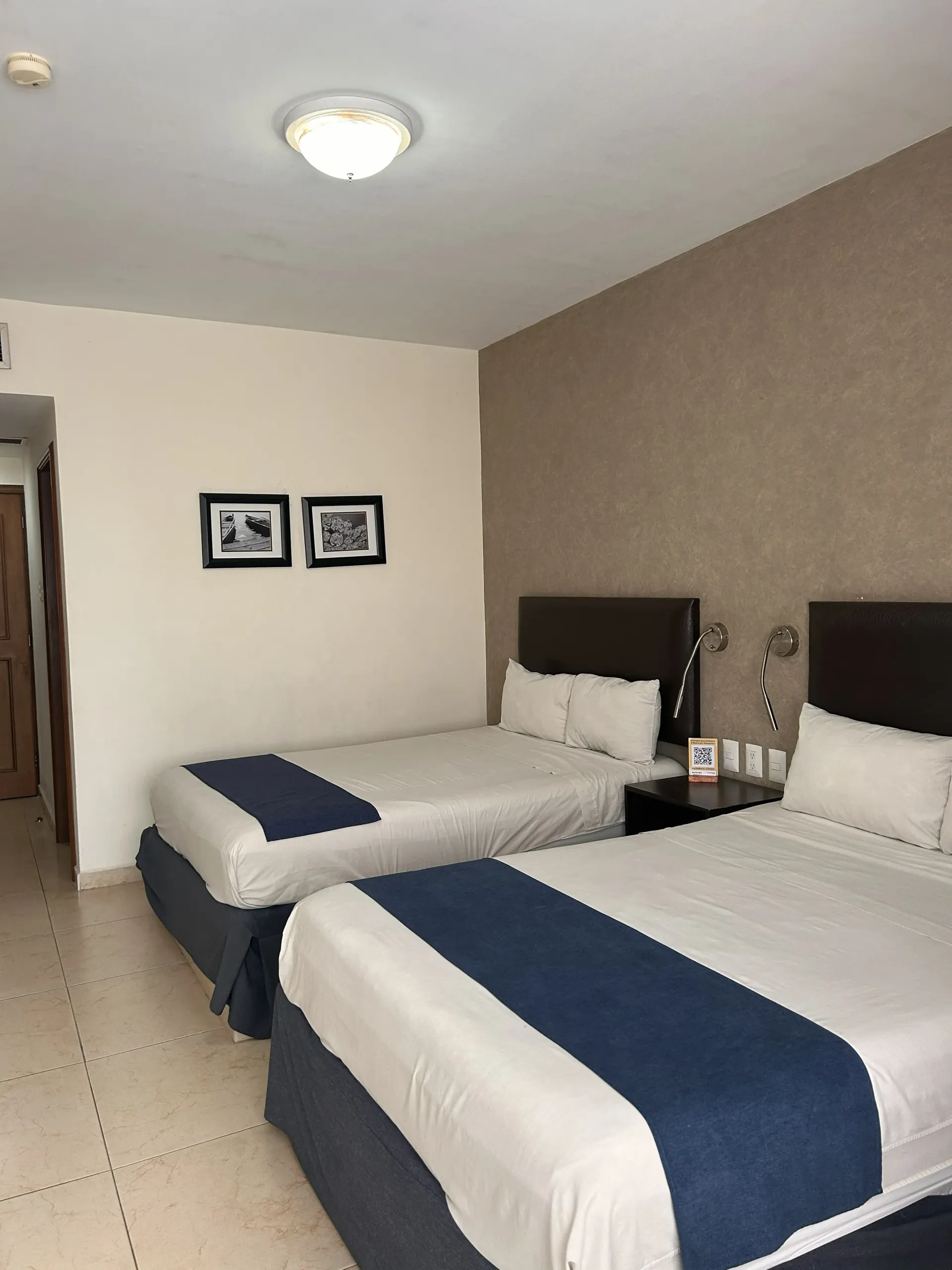 Una habitación de hotel con dos camas tamaño queen, sábanas blancas, caminos de mesa azules.