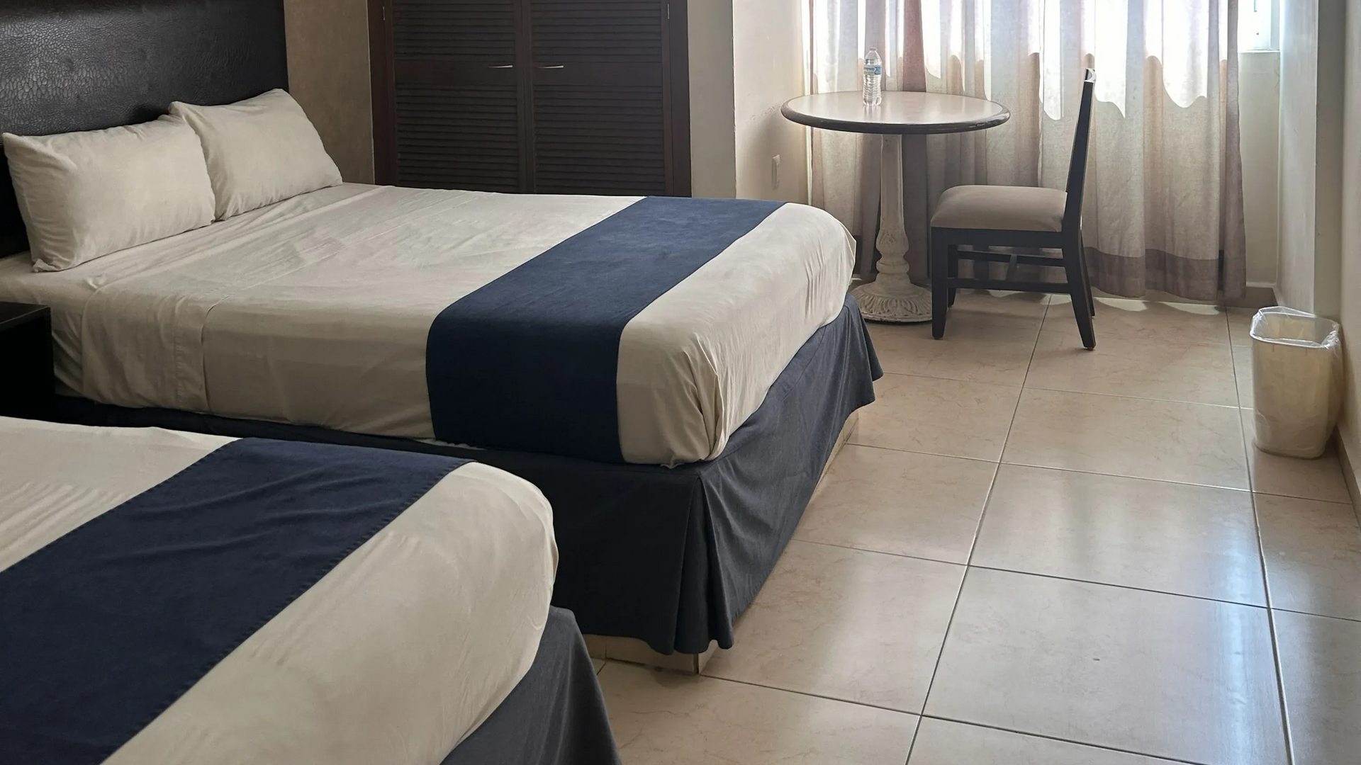Una habitación de hotel con dos camas con ropa de cama blanca y caminos de mesa azules.