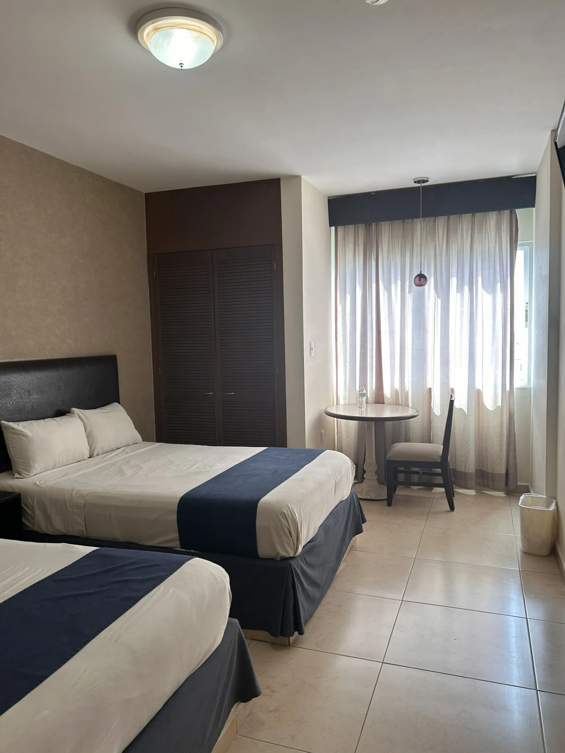 Una habitación de hotel con dos camas, un armario de color marrón oscuro, una pequeña mesa redonda.