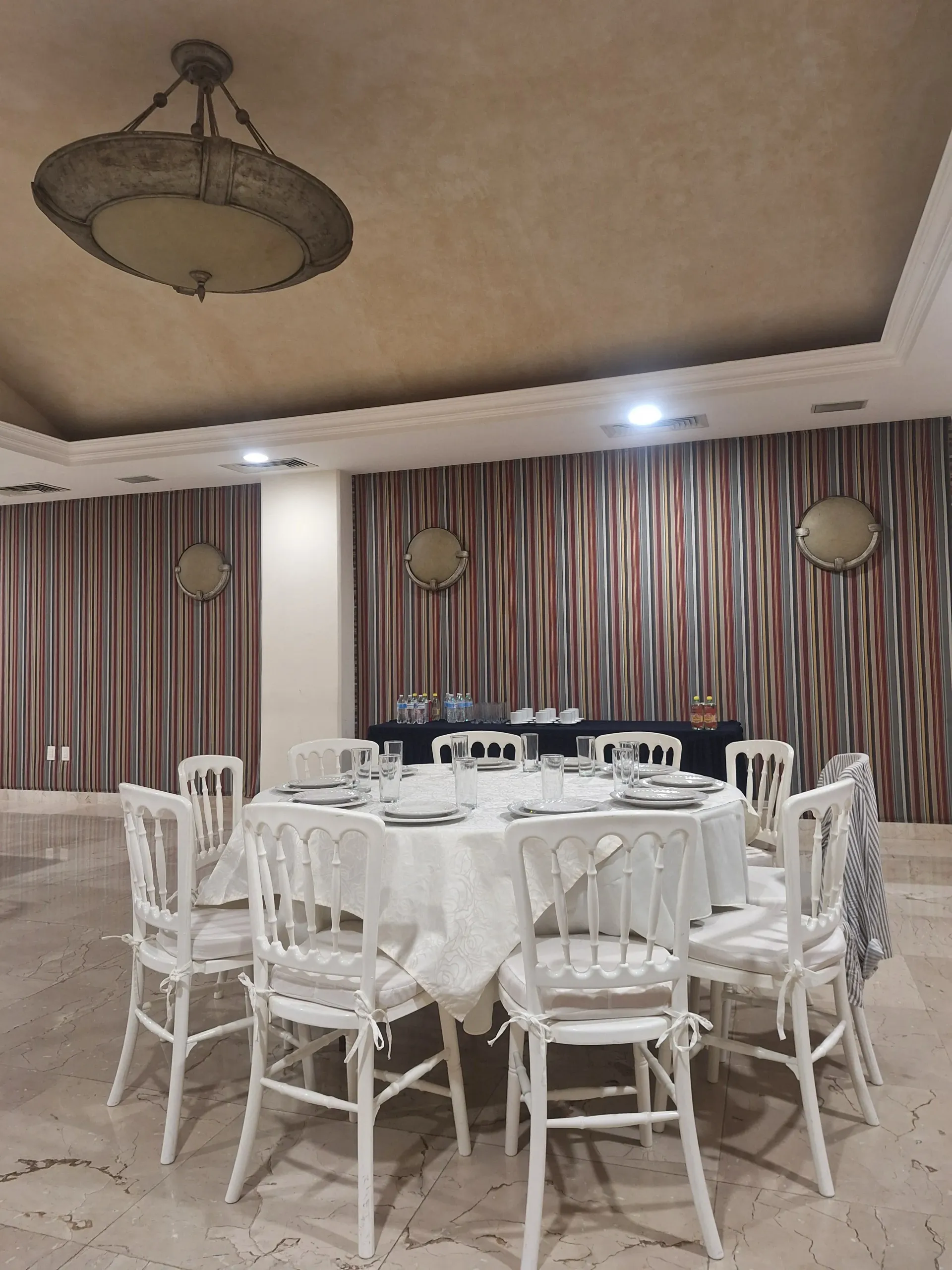 Una mesa redonda de banquete con mantel blanco y sillas dispuestas en un comedor con cortinas.