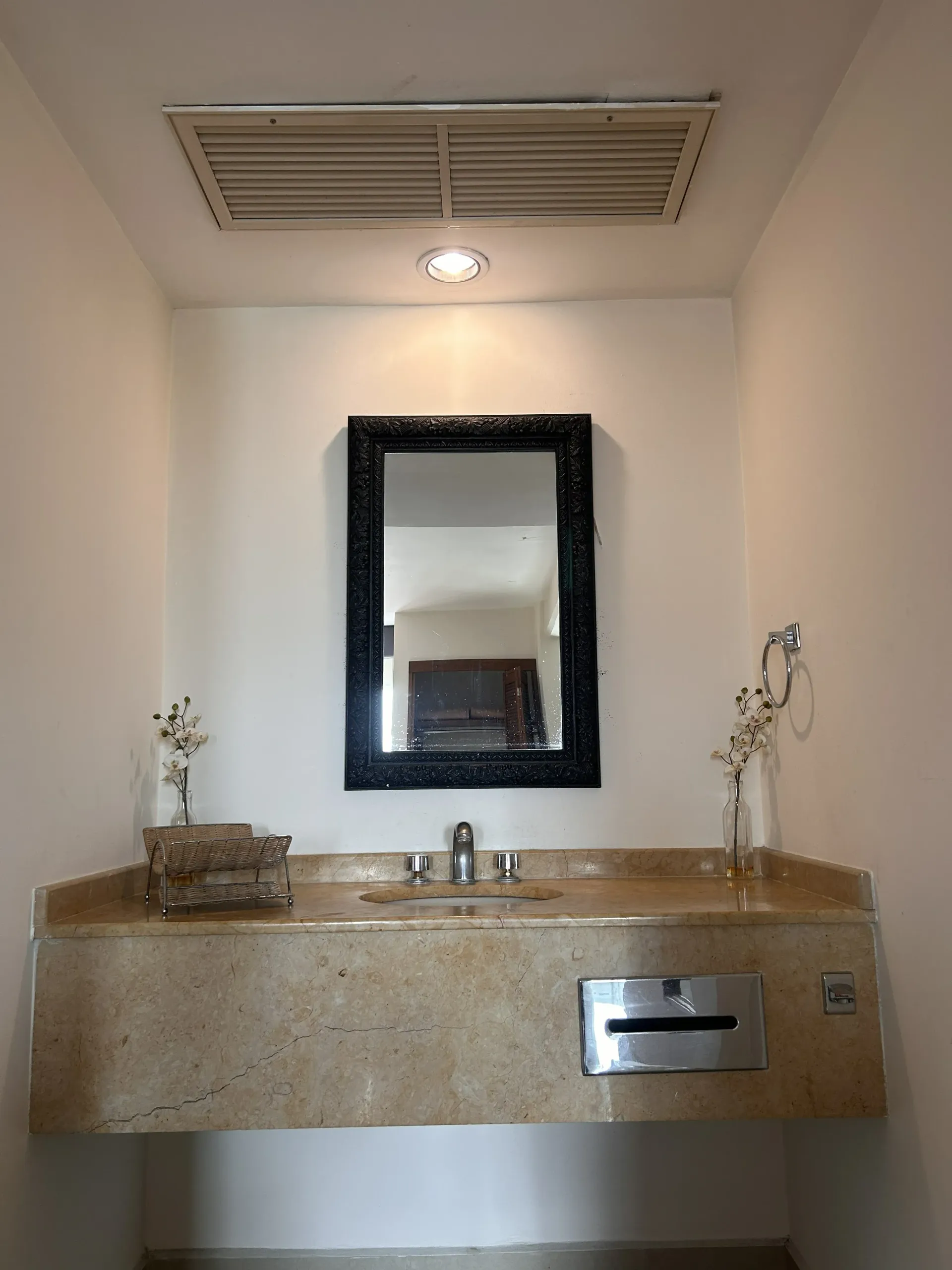 Un tocador con encimera de piedra beige, lavabo y espejo con marco negro.