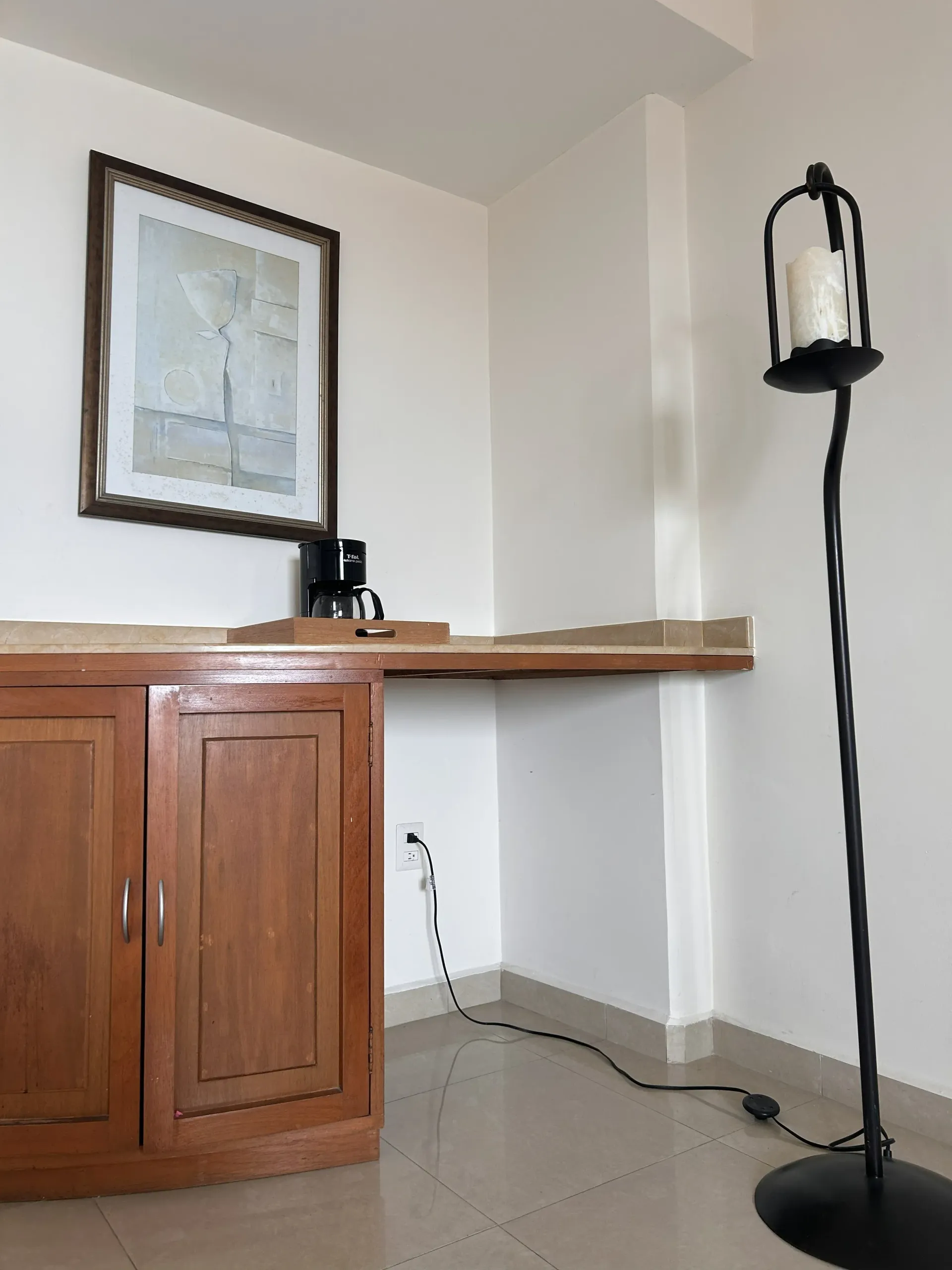 Un mueble de madera con una cafetera, un cuadro enmarcado en la pared de arriba y una lámpara.