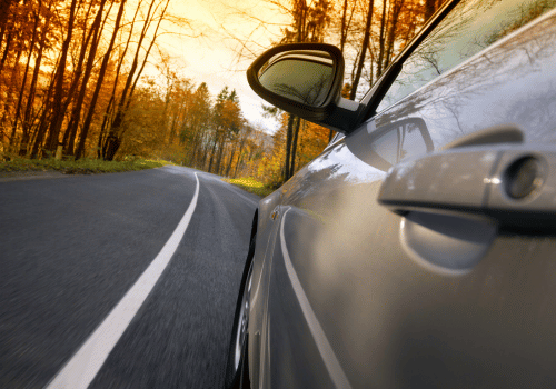 Car driving along a curving road beside autumn trees at sunset