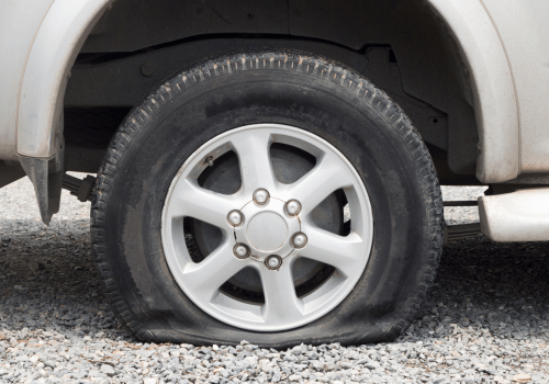 Close-up of a car’s front wheel and tire on gravel, with a flat tire visible