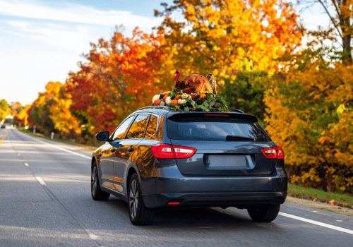 Black SUV driving on a tree-lined road with autumn foliage and luggage on the roof rack
