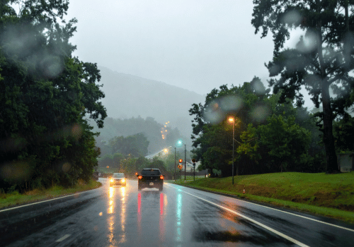 Cars driving on a wet road in heavy rain with headlights reflecting on the pavement.