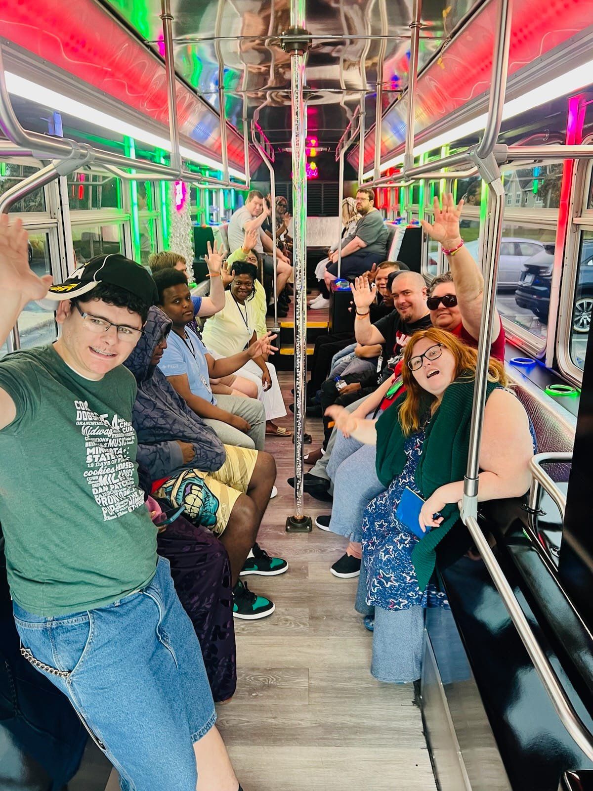 People waving inside a party bus with colorful lights.