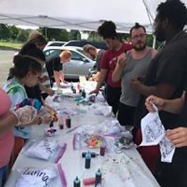 People tie-dyeing at a table outdoors. Shirts and supplies are visible.