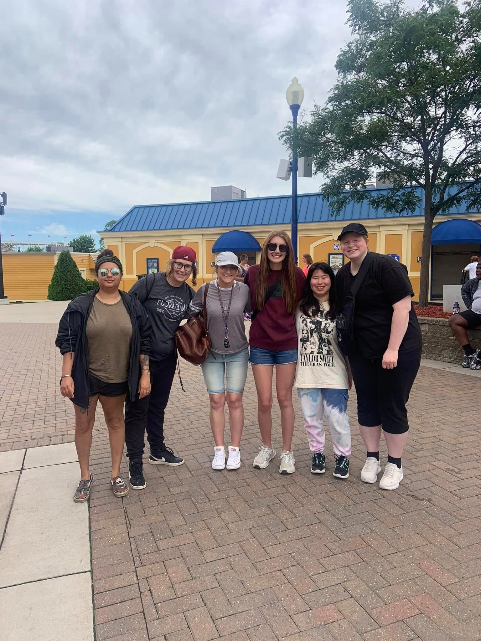 Group of six people posing outdoors in front of a blue-roofed building.