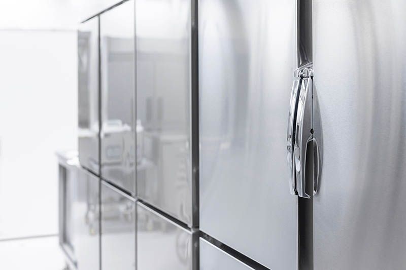 A row of stainless steel refrigerators in a kitchen.