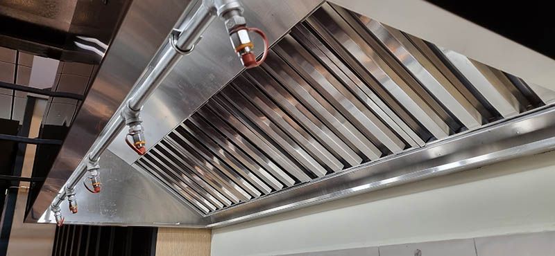 A stainless steel exhaust hood is hanging from the ceiling of a kitchen.