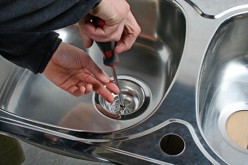 A person is fixing a sink with a screwdriver.
